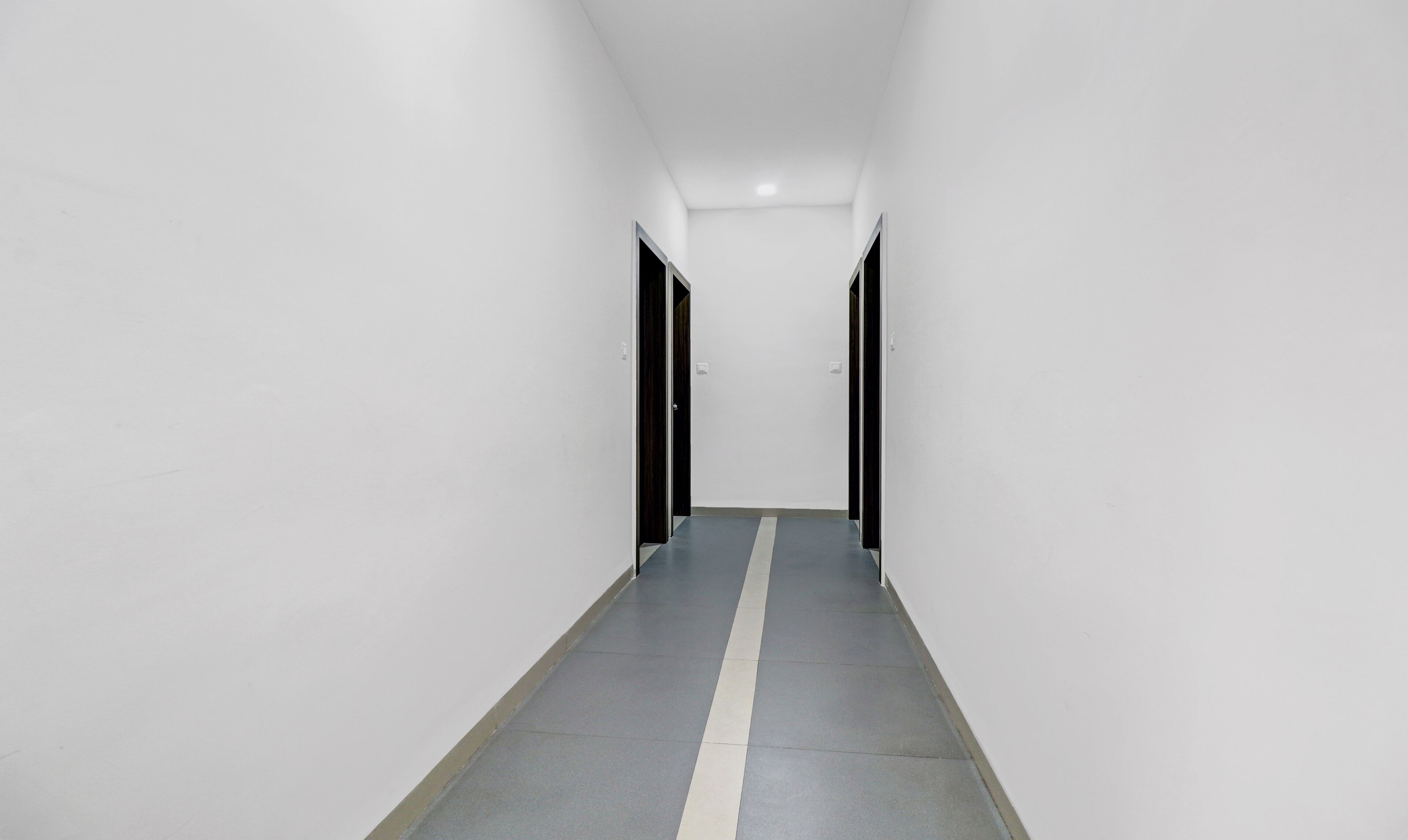 Un pasillo estrecho, bien iluminado, con paredes blancas y piso gris.