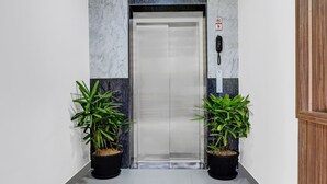 An elevator with a marble wall, a fire alarm, and two potted plants. - Treebo Raga (Visakhapatnam)