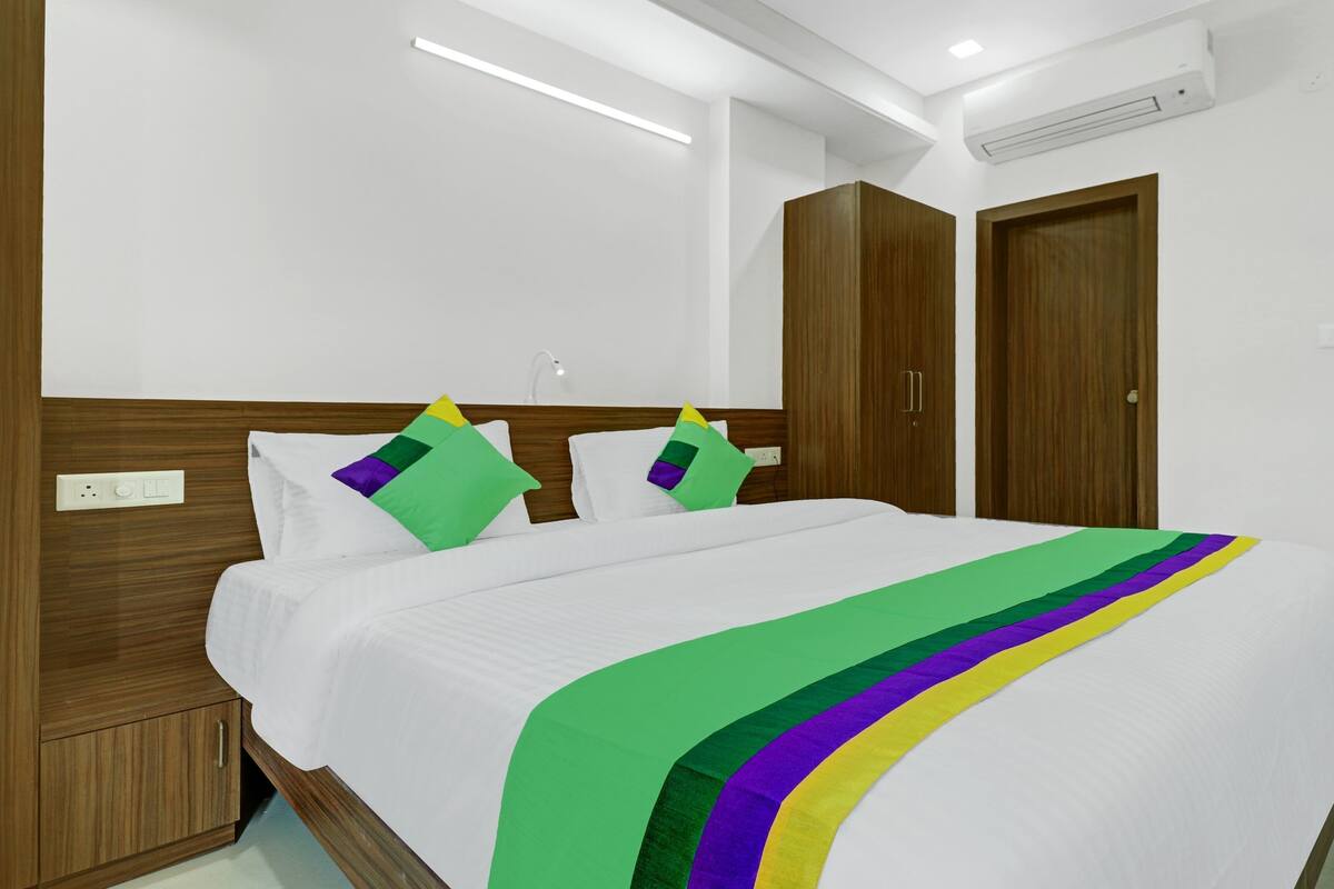 A hotel room with a bed, wooden wardrobe, and a white wall.