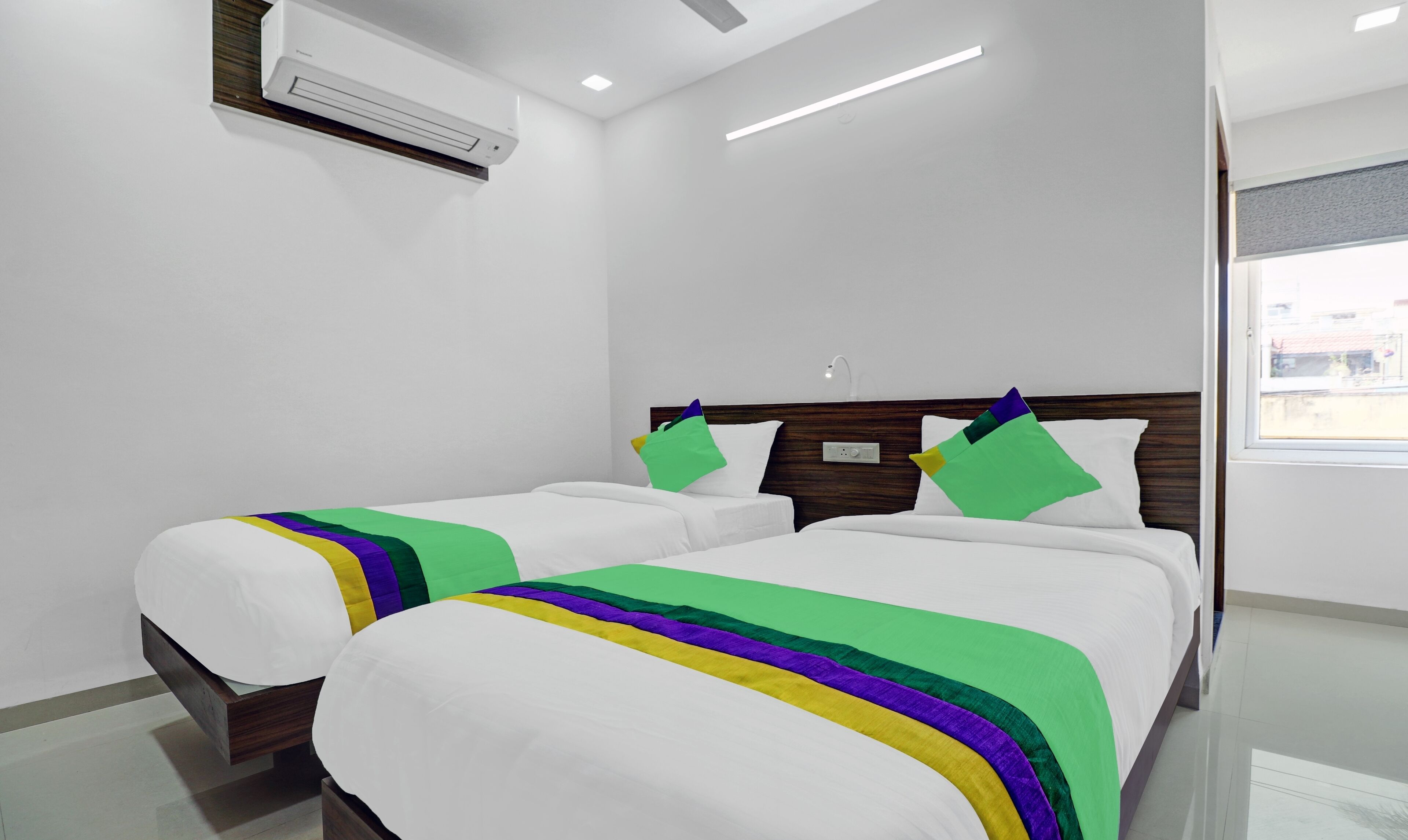 A hotel room with two beds, white bedding, a wooden headboard, an air conditioning unit, and a window with a view.