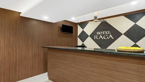 A hotel reception area with a wooden reception desk, a flat-screen TV mounted on the wall, and a sign that reads "HOTEL RAGA". - Treebo Raga (Visakhapatnam)