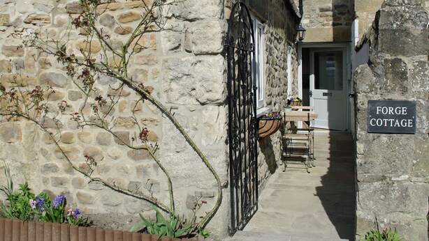 Une petite maison en pierre avec une pancarte indiquant « Forge Cottage ».