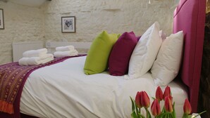 Un lit bien fait, avec une couette blanche, plusieurs oreillers de différentes couleurs et une tête de lit violette.