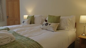 Ein Doppelbett mit weißen Bettwäsche, zwei grüne Kissen und ein gefaltetes weißes Handtuch daneben.