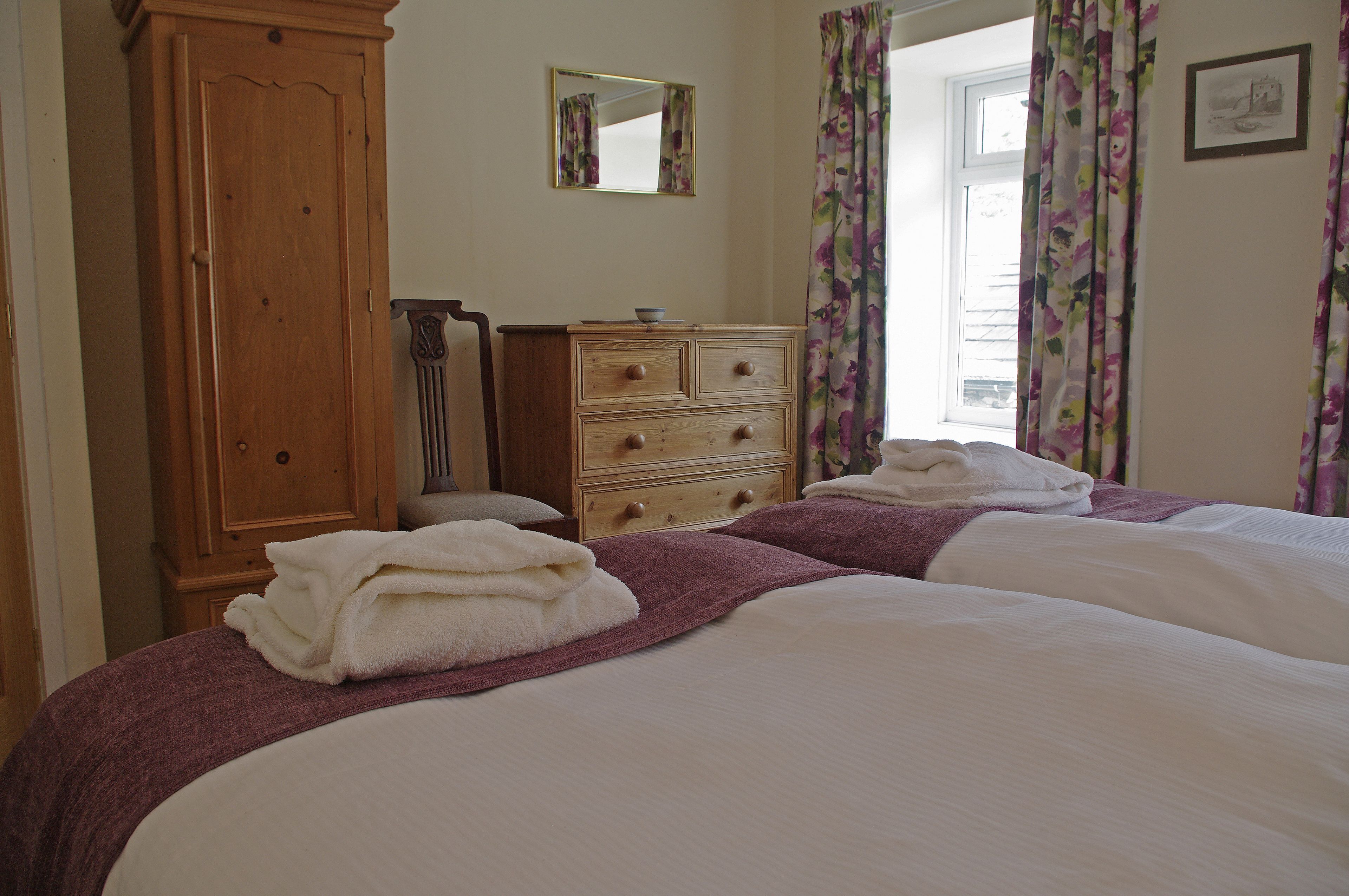 A bedroom with two beds, a wooden wardrobe, a mirror, and floral curtains.