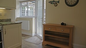 Eine Küche mit einem Holzkasten, einem Fenster mit Aussicht, einer Uhr und einem kleinen Holzregal.