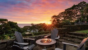 A sunset view with a fire pit and Adirondack chairs. - Hale Joli: Historic Hawaiian Home w/Ocean Views, Lanai & BBQ Area (Kailua-Kona)