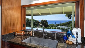 A kitchen with a large sink, wooden cabinets, and a view of the ocean. - Hale Joli: Historic Hawaiian Home w/Ocean Views, Lanai & BBQ Area (Kailua-Kona)