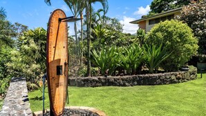 A stone pathway leading to a wooden structure with a water feature, surrounded by lush greenery and a house in the background. - Hale Joli: Historic Hawaiian Home w/Ocean Views, Lanai & BBQ Area (Kailua-Kona)