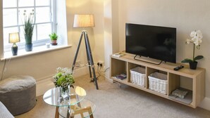 A living room with a TV, a tripod, a lamp, a glass table, and a sofa. - 1 bedroom accommodation in Helmsley (Helmsley)