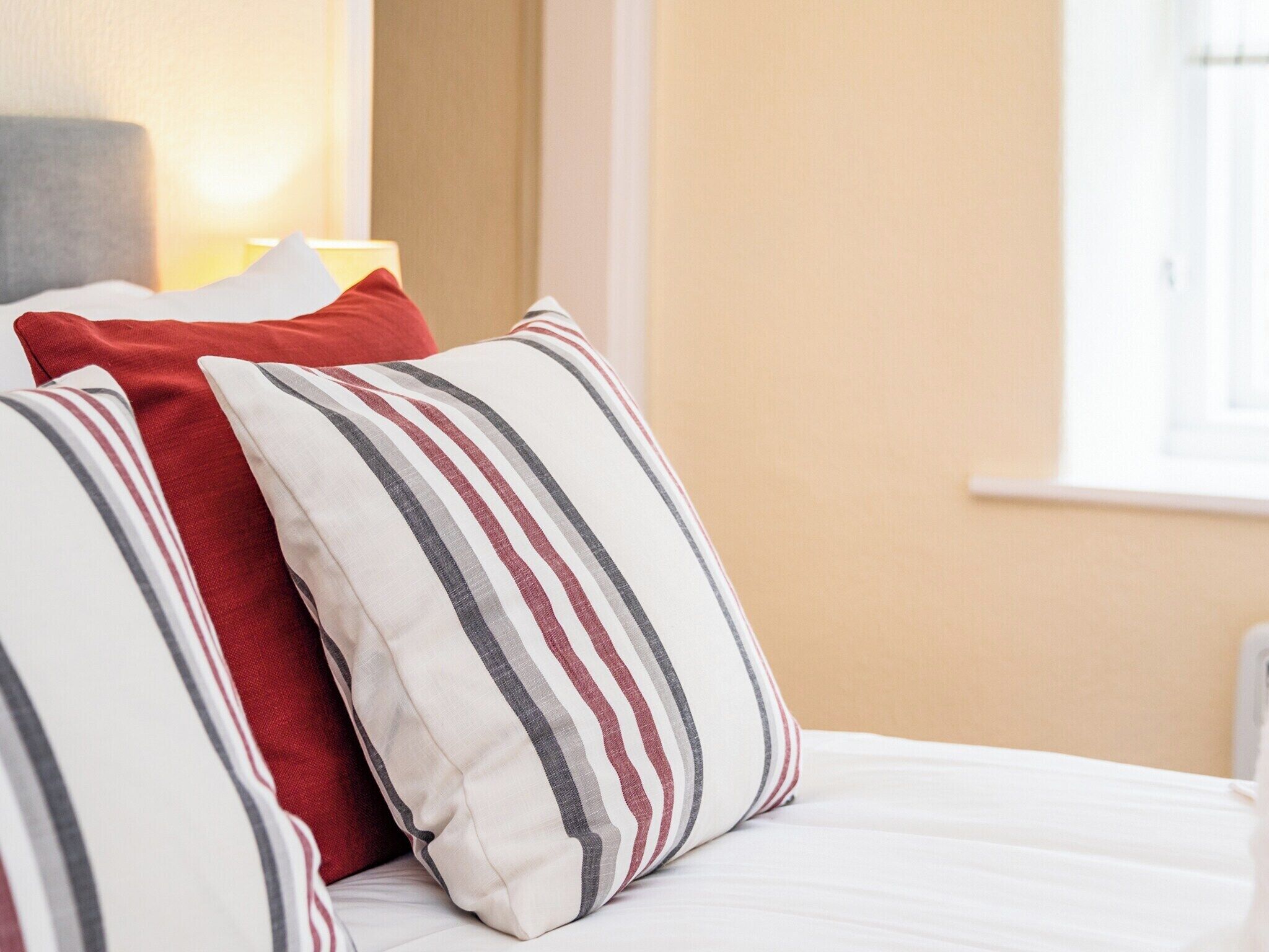 A bed with white bedding and striped pillows in red, gray, and white.