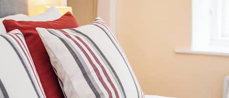 A bed with white bedding and striped pillows in red, gray, and white.