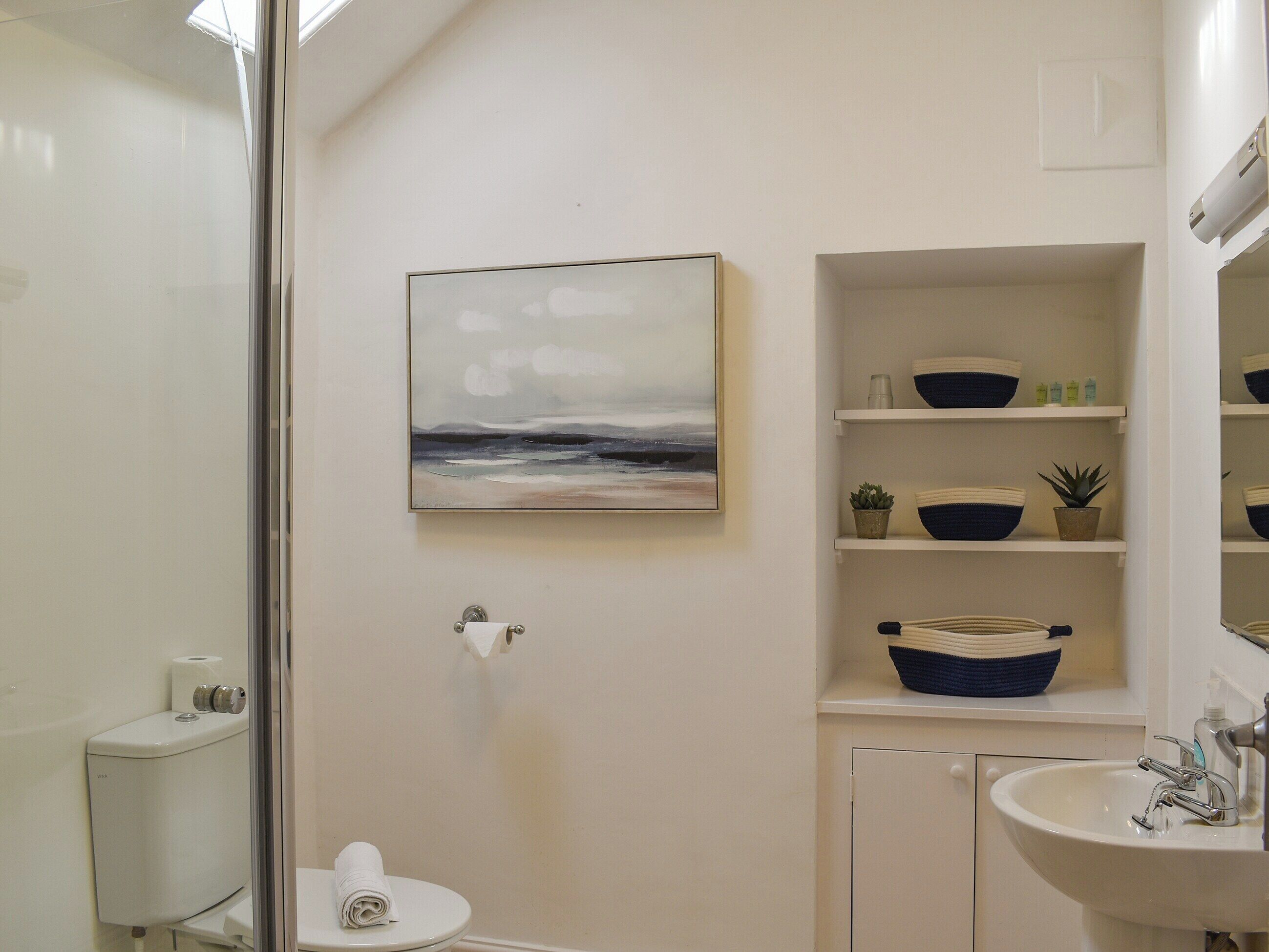 Baño con inodoro, lavabo y estantes con cuencos y plantas.