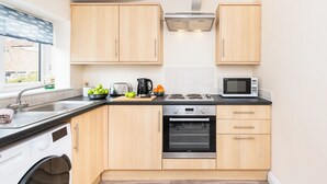 A modern kitchen with wooden cabinets, a built-in oven, a microwave, and a washing machine. - 1 bedroom accommodation in Helmsley (Helmsley)