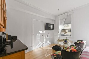 Een moderne keuken met een ingebouwde kookplaat, een eethoek met tafel en stoelen, en een aan de muur bevestigde televisie.