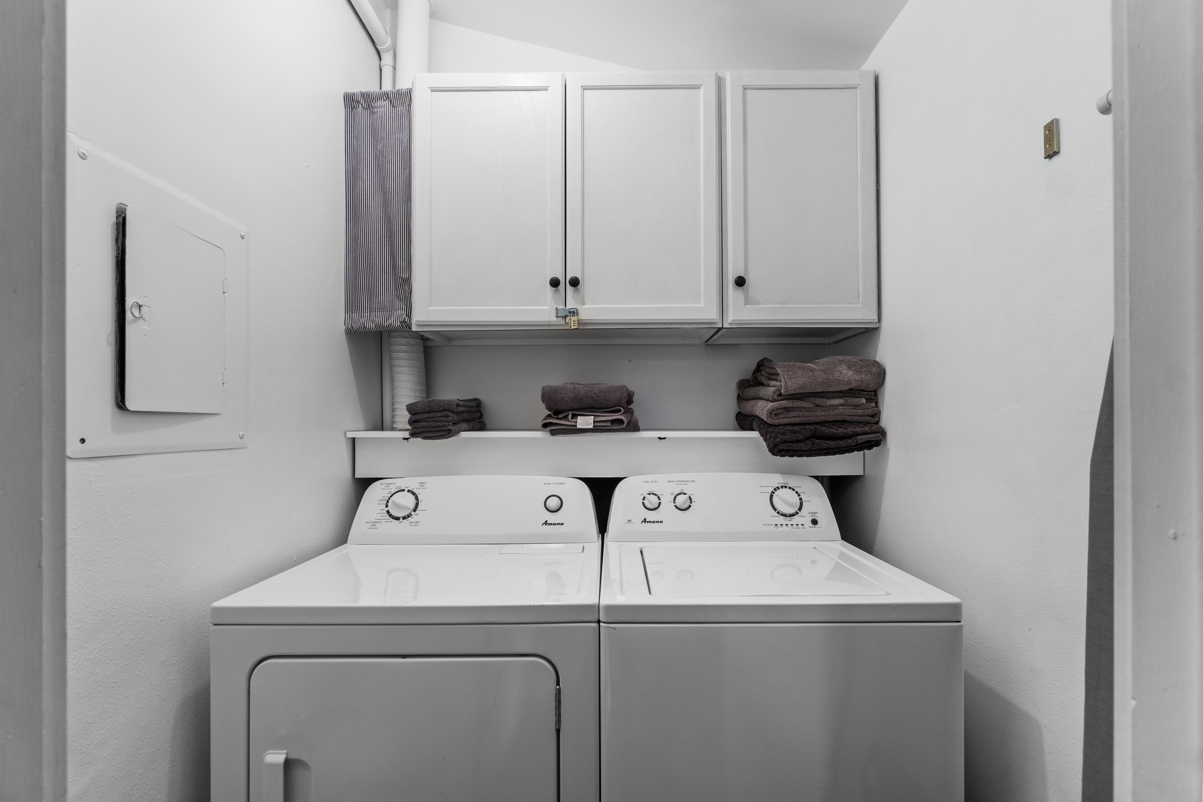 A compact laundry area with two washing machines, a drying rack, and a cabinet above.