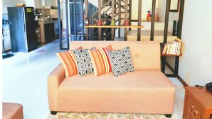A living room with a sofa, pillows, a bookshelf, and a staircase leading to an upper level.