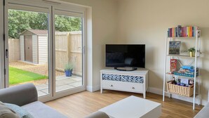 A living room with a TV, sofa, and a bookshelf with books and games. - 3 bedroom accommodation in Buxton (Buxton)
