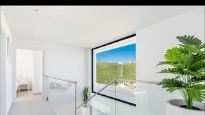 Un interno moderno con una scala in vetro, una grande finestra con vista sul verde e una pianta in vaso.