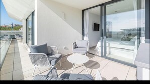 Un balcone moderno con arredi bianchi, una porta in vetro che dà su una terrazza e una vista aperta sulla città.