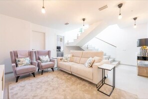 Ein modernes Wohnzimmer mit einem beigen Sofa, zwei Sesseln, einem Couchtisch und einer Treppe.