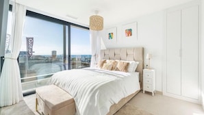 Una camera da letto moderna con un letto grande, un comodino, un armadio e vista sulla città attraverso ampie finestre.