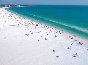 Ein Strand mit vielen Sonnenschirmen und Menschen, einem klaren blauen Meer und einem weiten Sandstrand.