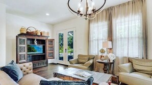 Een woonkamer met een bank, fauteuils, een salontafel, een televisie en een kroonluchter.