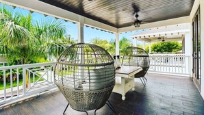 Een overdekte terras met houten plafond, twee metalen bolvormige stoelen, een tafel en een witte balustrade.