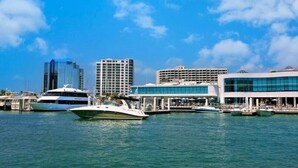 Een jachthaven met verschillende jachten, moderne gebouwen met grote ramen en een heldere blauwe lucht.