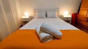 A neatly made bed with white linens and a rolled towel, two bedside lamps, and a wooden wardrobe. - Paradise By The Sea - TheWhaleBeachHouse (Atouguia da Baleia)