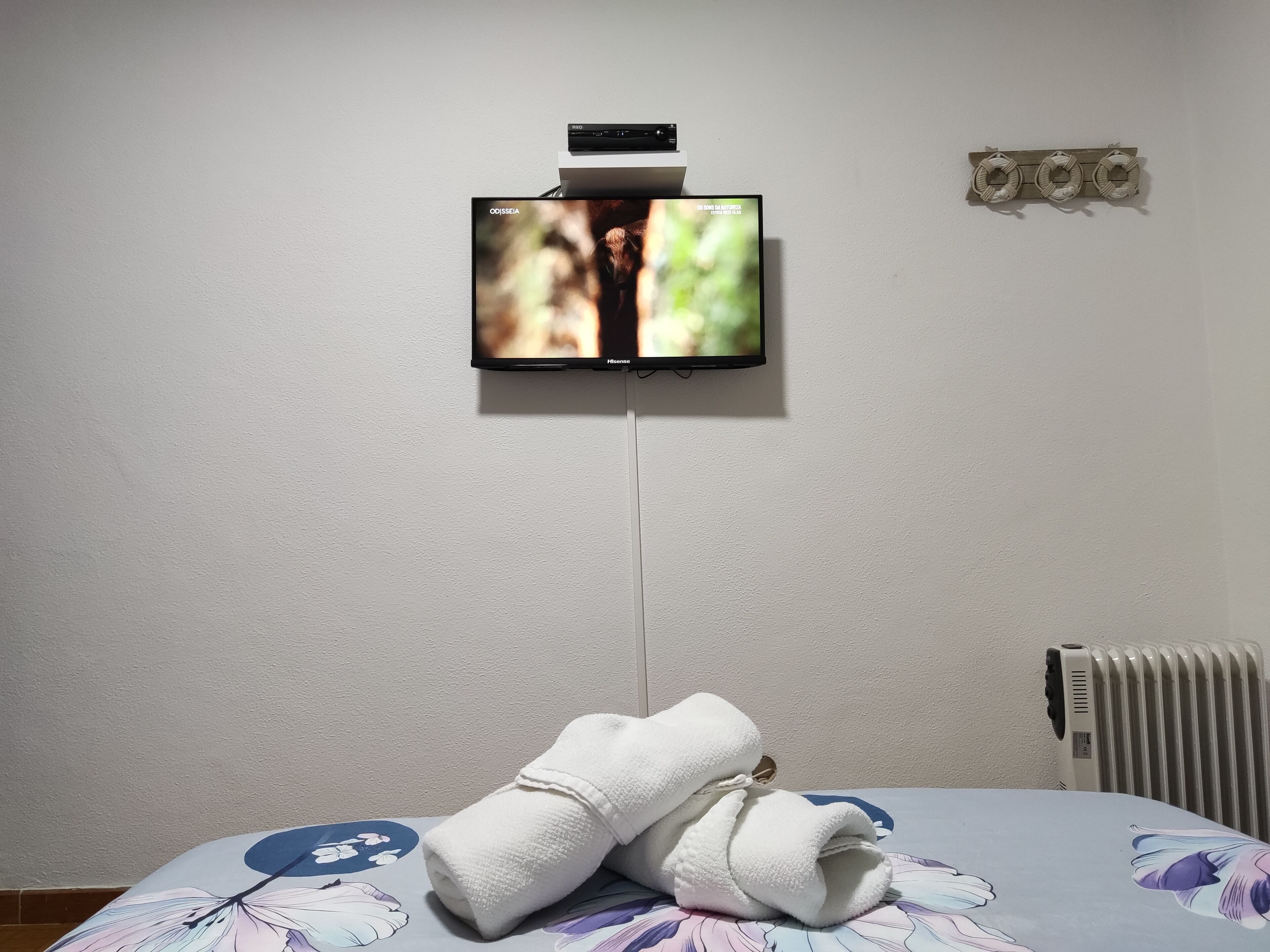 A television mounted on a wall, a radiator, and a bed with a floral bedspread.