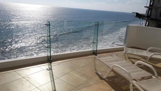 A balcony with a view of the ocean, two white chairs, and a glass railing. - Condos Ventana R (Mazatlán)