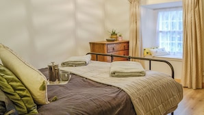A bedroom with a bed, bedside table, and a window with curtains. - Full of character, this cosy cottage is in a quiet lane in a charming village. (Perth)