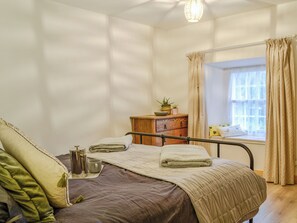 Un dormitorio con cama, mesita de noche y ventana con cortinas.