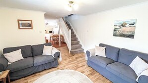 A living room with two sofas, a rug, a staircase, and a dining area in the background. - Full of character, this cosy cottage is in a quiet lane in a charming village. (Perth)