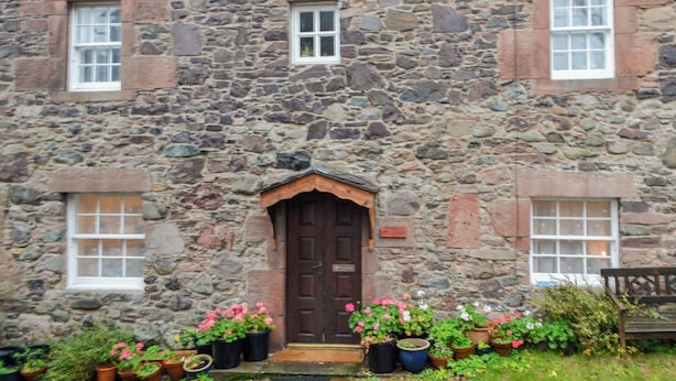 A stone building with a central door, two windows on either side, and potted plants in front. - Full of character, this cosy cottage is in a quiet lane in a charming village. (Perth)
