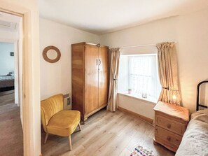 Una habitación con armario, silla, ventana con cortinas, cómoda y radiador.