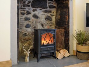 A stone fireplace with a modern wood-burning stove, a decorative deer head, and a potted plant.