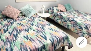 Una habitación con dos camas, cada una con ropa de cama estampada y almohadas decorativas. Hay una pequeña mesa redonda con una lámpara entre las camas.