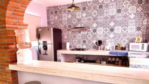 Una cocina con salpicadero estampado, un refrigerador, un microondas y una encimera de madera. Hay tres taburetes y una lámpara colgante.