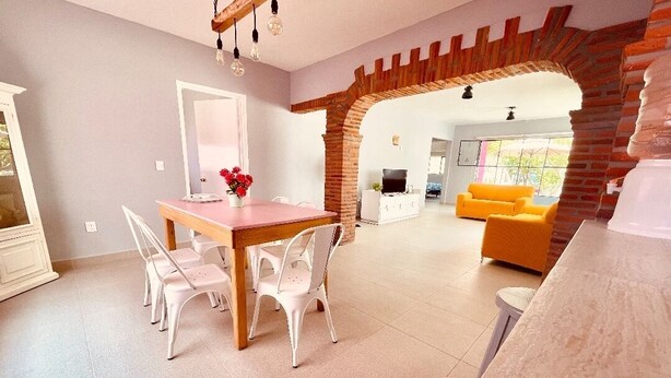 Amplia sala de estar con una mesa y sillas de comedor, un sofá amarillo brillante y un arco de ladrillo que conduce a otra habitación.