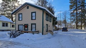 A two-story building with a snow-covered driveway and steps leading to the entrance. - Stay near Mirror Lake, enjoy our cozy 2-bedroom cottage (Lake Placid)