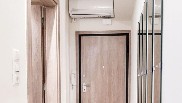 A hallway with a wooden door, an air conditioning unit above it, and a wall-mounted mirror on the right. - Byronico Acropolis Apartment by MPS (Αθήνα)
