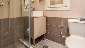 A bathroom with a glass shower enclosure, a white sink, a mirror, and a toilet. - Byronico Acropolis Apartment by MPS (Αθήνα)