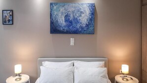 A bedroom with a bed, two bedside tables with lamps, a wall-mounted painting, and a small framed picture. - Byronico Acropolis Apartment by MPS (Αθήνα)