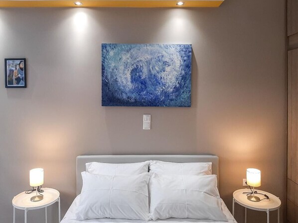 Une chambre à coucher avec un lit, deux tables de chevet avec des lampes, un tableau accroché au mur et un petit tableau encadré.