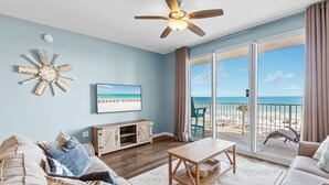 Ein Wohnzimmer mit Blick auf den Strand, einem Deckenventilator, einem Fernseher und einem Holzkasten.