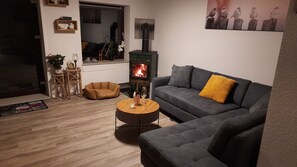 Un salon chaleureux avec un canapé gris, une petite table basse ronde en bois, un panier pour chien, une cheminée et un miroir au mur.