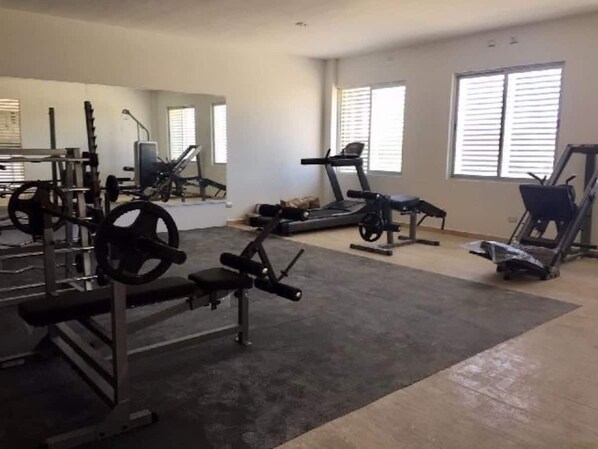 Et fitnesscenter med forskellig træningsudstyr, herunder løbebånd og styrkemaskiner, i et rummeligt lokale med store vinduer.
